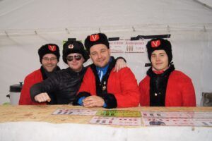 Vier Personen in roten Jacken und schwarzen Mützen lächeln.