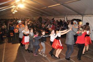 Kinder und Erwachsene tanzen zusammen im Zelt. Sie tragen traditionelle Kleidung.