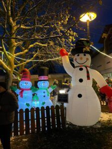 Ein großer aufblasbarer Schneemann neben einem kleinen Zaun und zwei kleineren Schneemännern.